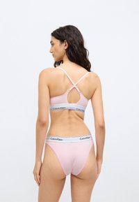 Ανοιχτό ροζ μπουστάκι με ρυθμιζόμενους ιμάντες και διασταυρούμενο σχέδιο, σετ με τανγκάκι που ταιριάζει, και τα δύο με σήμανση Calvin Klein.