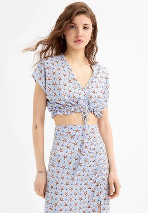 Top corto azul y falda a juego con un patrón de rayos de sol. Tejido texturizado con detalles fruncidos. Se ata en la cintura y tiene mangas cortas.