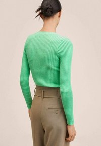 Ribbed grüner Pullover mit langen Ärmeln, runder Halslinie und strukturierter Oberfläche, kombiniert mit beigen maßgeschneiderten Hosen mit einer Gesäßtasche.
