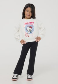 Felpa bianca a maniche lunghe con grafica di Hello Kitty, leggings neri e sneakers nere con accenti bianchi. Tessuto morbido e polsini aderenti.