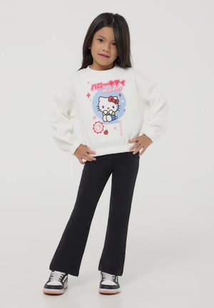 Felpa bianca a maniche lunghe con grafica di Hello Kitty, leggings neri e sneakers nere con accenti bianchi. Tessuto morbido e polsini aderenti.