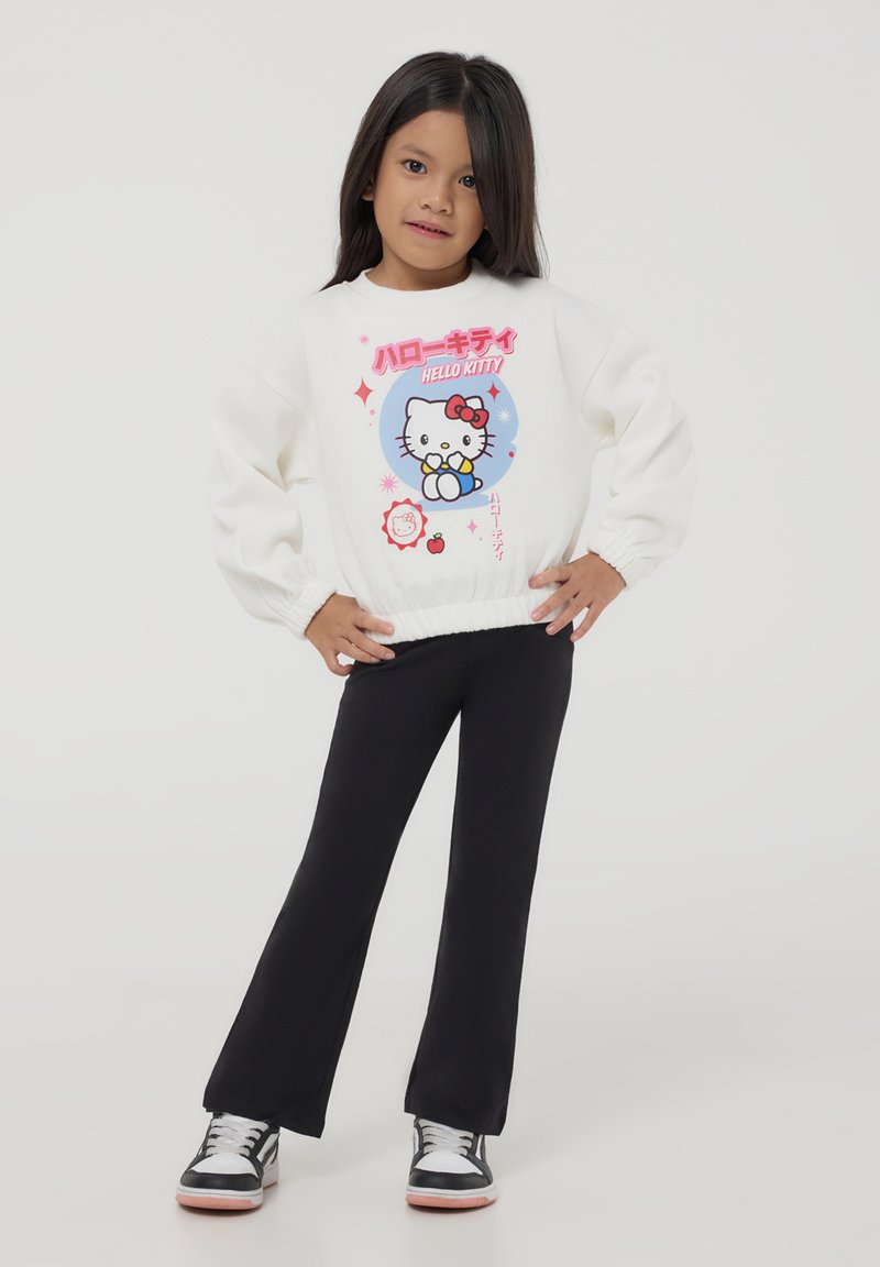 Felpa bianca a maniche lunghe con grafica di Hello Kitty, leggings neri e sneakers nere con accenti bianchi. Tessuto morbido e polsini aderenti.
