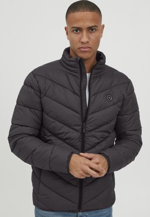 Padded jacket in dark gray, featuring a zip closure, high collar, chevron pattern, and a small logo emblem on the left chest area.