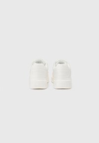 White sneakers with smooth synthetic upper, rounded design, padded collar, and textured rubber sole. Minimalistic style with subtle branding.