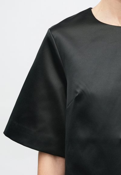 Haut court en satin noir à manches courtes, avec un col rond, une texture lisse et une coupe décontractée. Conception sans coutures, sans éléments visibles ni motifs.
