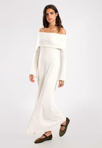 Langes, schulterfreies weißes Kleid aus weichem Stoff, mit langen Ärmeln und fließender Silhouette, kombiniert mit grünen Ballerinas.
