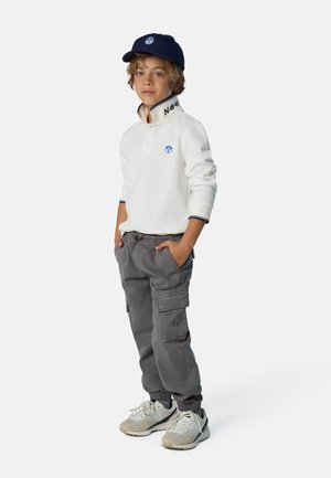 Weißes Langarm-Polo mit Knopfleiste und blauem Logo, kombiniert mit grauen Cargo-Hosen und hellgrauen Sneakern. Eine marineblaue Cap rundet das Outfit ab.