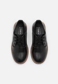 Chaussures en cuir noir à lacets avec un bout arrondi, contrastées par une semelle brune cousue. Conçues pour le confort et la polyvalence.