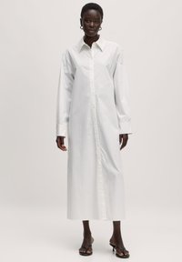 Langes weißes Hemdkleid mit Kragen, durchgehender Knopfleiste und langen Ärmeln. Hergestellt aus glattem Stoff mit gerader Silhouette.