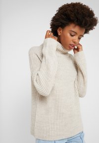 Beige ribbed turtleneck sweater with a relaxed fit and long sleeves, made from a soft knit material. Casual cut, minimal design.
