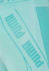 Leggings sportivi di un azzurro chiaro con un tessuto testurizzato, audace branding diagonale "PUMA" e linee di accento lisce in una tonalità leggermente più scura.