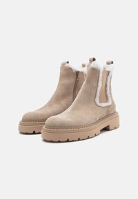 Bottes d'ankle en suède beige avec doublure en fausse fourrure blanche, panneaux latéraux élastiques et semelles en caoutchouc épaisses. Détails de couture le long de la semelle.