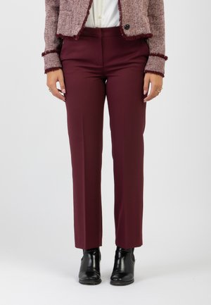 Pantaloni su misura borgogna con una texture liscia, design a gamba dritta, indossati sopra stivaletti neri alla caviglia, abbinati a una blusa chiara.