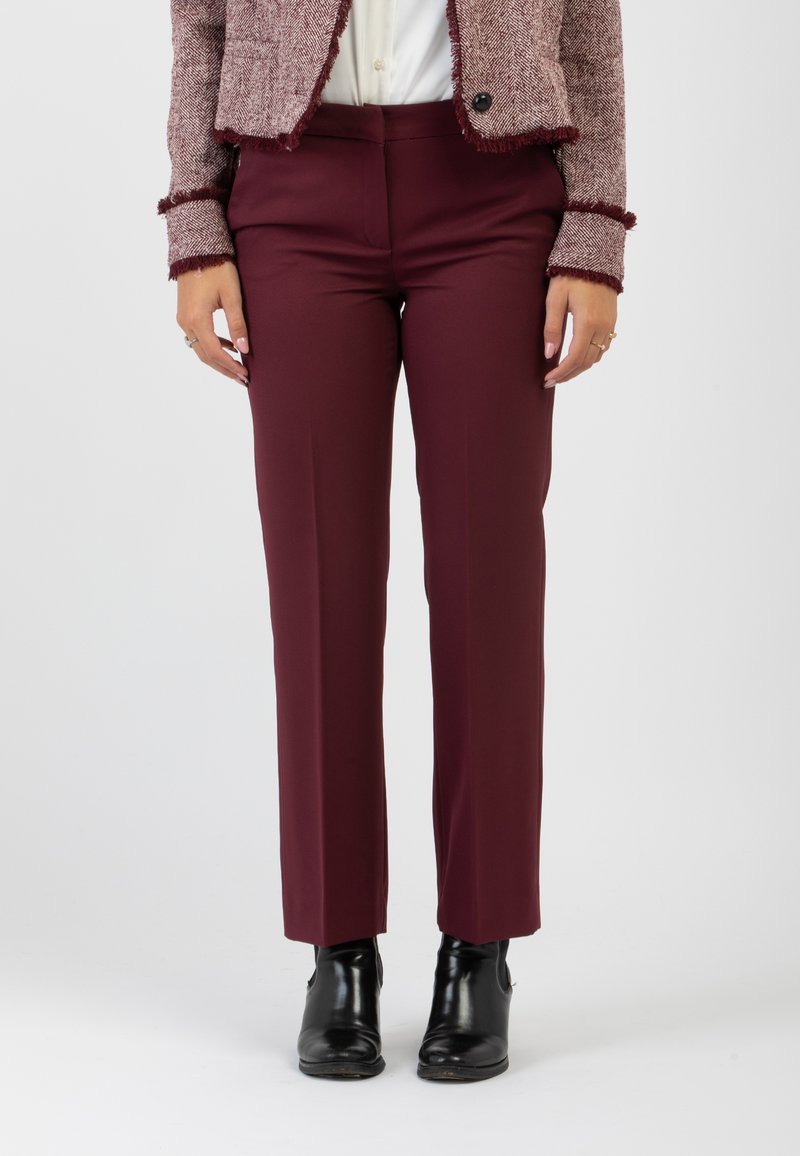 Pantaloni su misura borgogna con una texture liscia, design a gamba dritta, indossati sopra stivaletti neri alla caviglia, abbinati a una blusa chiara.