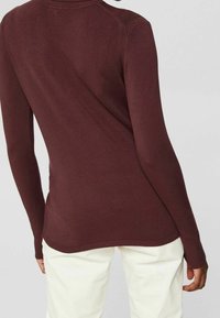 Maglione bordeaux a maniche lunghe con collo alto, caratterizzato da polsini e orlo a coste. Tessuto liscio, design aderente e dettagli di cuciture sottili.