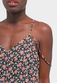 Haut à impressions florales sur fond noir, avec des bretelles fines et réglables, un décolleté en V et de petits motifs colorés de fleurs.