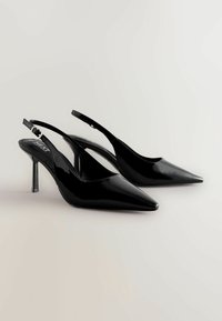 Fekete lakk bőr slingback magassarkú cipők hegyes orral, vékony magas sarkakkal és állítható pánttal. Simaságával és fényes felületével tűnik ki.