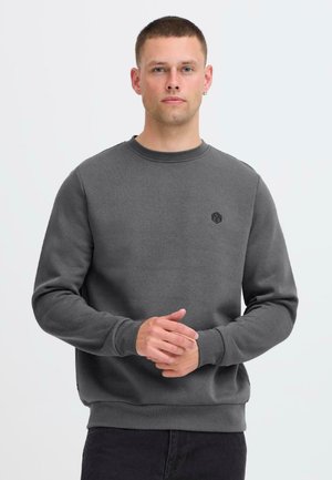 Grå sweatshirt i mjukt tyg med rundhals och långa ärmar. En liten svart logga är broderad på bröstet.