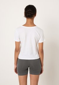 Weißes T-Shirt aus Baumwolle mit kurzen Ärmeln, einem runden Ausschnitt und lockerem Sitz, kombiniert mit dunkelgrauen, figurbetonten Shorts.