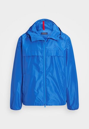 Blue lightweight jacket with a zip front, adjustable hood, and dual side pockets. Features a smooth, shiny texture and logo detail on chest.