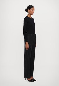 Haut noir à manches longues associé à un pantalon à rayures verticales taille haute. Le modèle porte des talons noirs à bout pointu. Design simple avec des détails minimalistes.