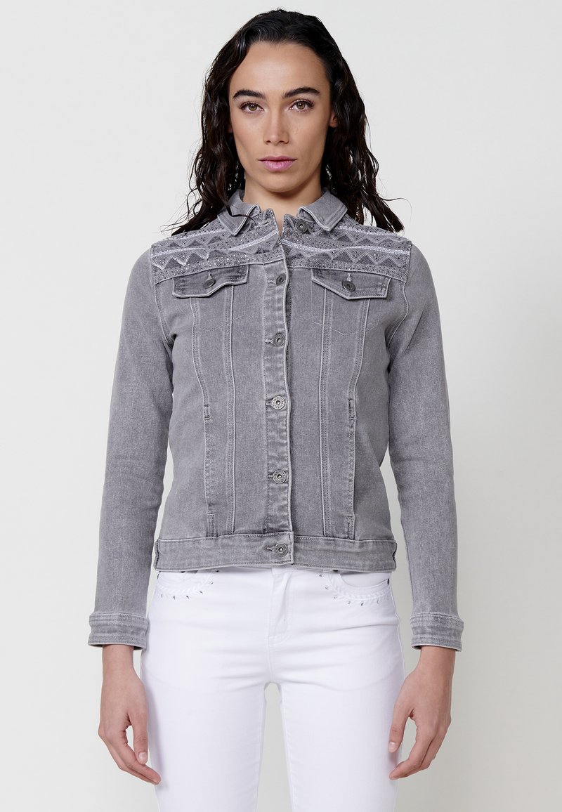 Siva denim jakna z oprijetim krojem, ki ima podrobno vezeno yoko, dve prsni žep in gumbasto zapiranje.