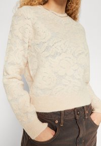 Hellbeiger gestrickter Pullover mit floralem Muster, gerippten Bündchen und Saum, zeichnet sich durch eine weiche Textur und einen Rundhalsausschnitt aus.