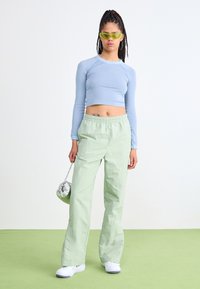 Top corto de rayas azul claro, pantalones holgados verde pálido, zapatos blancos, bolsa plateada y gafas de sol verdes. Texturas suaves y ajuste relajado.