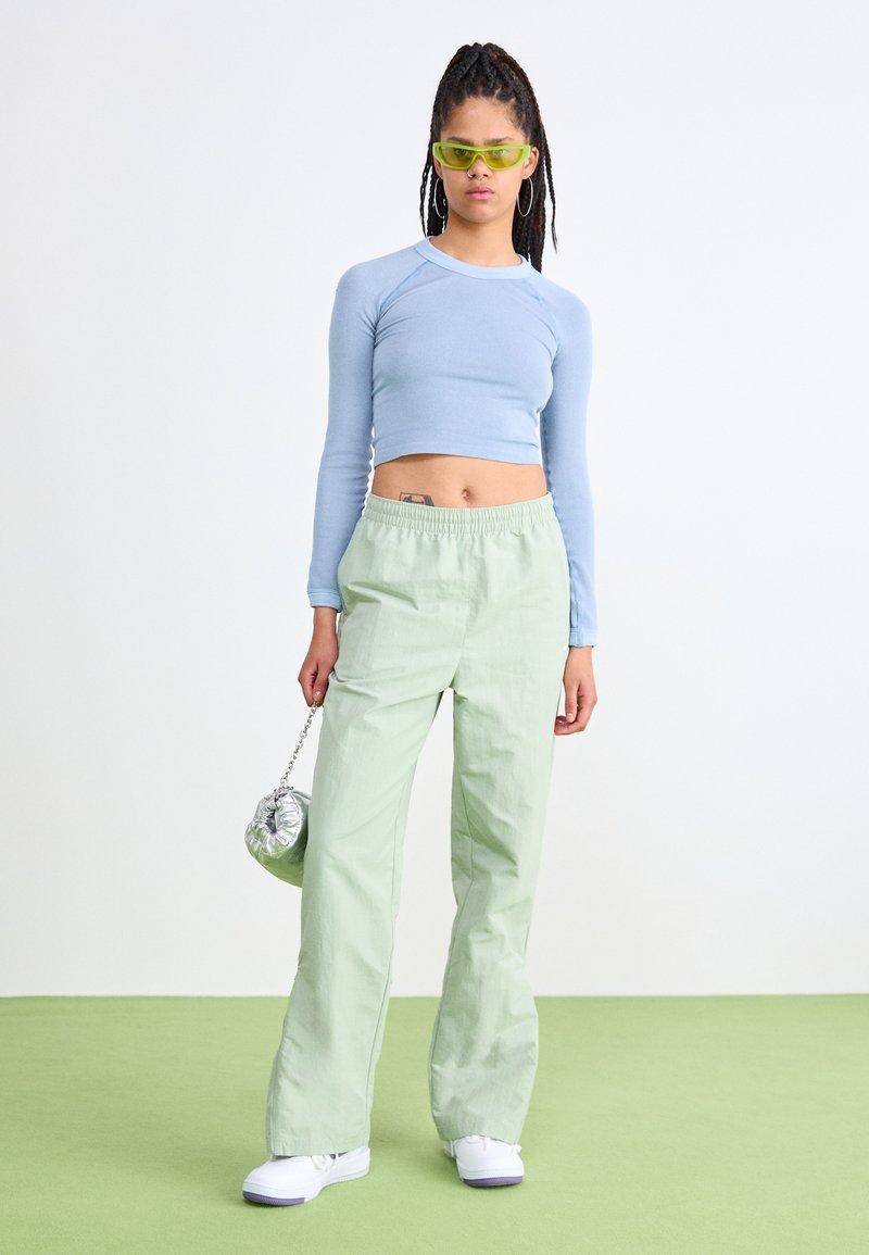 Top corto de rayas azul claro, pantalones holgados verde pálido, zapatos blancos, bolsa plateada y gafas de sol verdes. Texturas suaves y ajuste relajado.