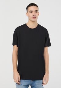 T-shirt nera a maniche corte con collo tondo, caratterizzata da una texture liscia e un design a taglio dritto. Abbinata a jeans chiari strappati.