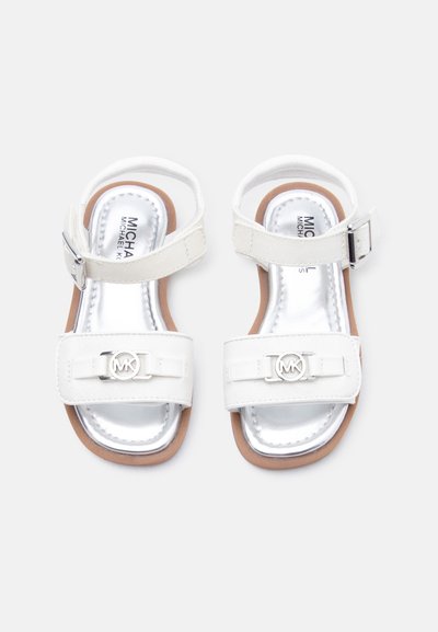 Λευκά πέδιλα παιδικά με λουριά στον αστράγαλο, ασημένιο λογότυπο Michael Kors στα εμπρόσθια λουριά και καφέ σόλες, εμφανίζονται από πάνω.