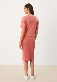 Ružový croptop s krátkymi rukávmi v kombinácii s priliehavou midi sukňou. Modelka má na sebe biele tenisky. Hladká textúra, neformálny dizajn.