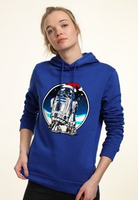 Blå hoodie med R2-D2 grafik iförd en julhatt, mot en cirkulär snötemat bakgrund. Tillverkad av mjukt tyg med en dragsko vid huven.