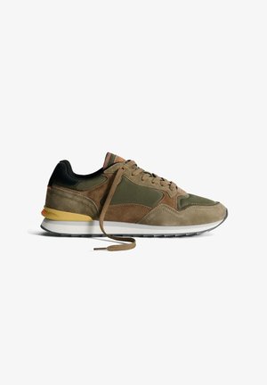 Sneaker scamosciato verde oliva e marrone con un retro nero, accenti beige e suola in gomma. Presenta lacci piatti e elementi di design sovrapposti.