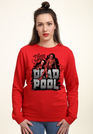 Kobieta z długimi brązowymi włosami w kok nosi czerwoną bluzę Deadpool z grafiką i napisem „Wygląda jak oskubiony indyk.”