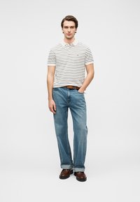 Ριγέ πόλο μπλουζάκι σε κρεμ και ναυτικό μπλε, σε συνδυασμό με ανοιχτό μπλε τζιν παντελόνι με ίσια γραμμή. Καφέ ζώνη και σκούρα καφέ παπούτσια ολοκληρώνουν το ντύσιμο.