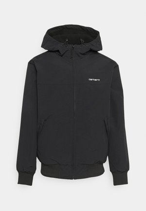 Veste à capuche zippée noire en tissu léger, dotée d'une capuche ajustable, de poignets côtelés et d'un petit logo blanc sur la poitrine.