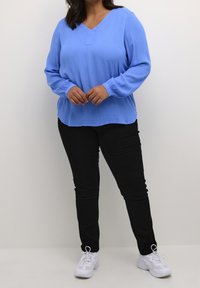 Blusa de manga larga azul claro con escote en V y una textura sutil, combinada con pantalones negro ajustados y zapatillas deportivas blancas.