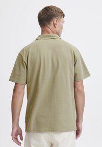 Kortermet polo shirt i olivengrønn bomull, med klassisk krage og avslappet passform, synlige stikninger ved kanten.