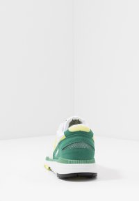 Scarpa da ginnastica verde e gialla con suola intermedia bianca, pannelli in rete, accenti testurizzati e tallone imbottito per il comfort.