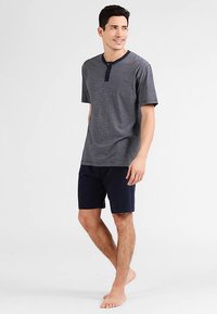 Marineblau gestreiftes Henley-Shirt mit kurzen Ärmeln und drei Knöpfen, kombiniert mit marineblauen Shorts. Baumwollstoff, lockere Passform und schlichtes Design.