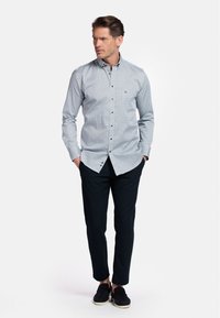Lichtblauwe overhem naar met geometrisch patroon, lange mouwen en een kraag. Gecombineerd met donkere broek en zwarte schoenen.
