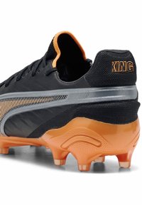 Svart fotbollssko med orange accenter, strukturerat mesh och ett glänsande silverfärgat designelement. Har en gummisula med dubbat grepp.