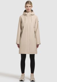 Beige waterdichte jas met een capuchon, ritszakken aan de zijkant en een minimalistisch ontwerp. Glad textuur, knielang, en drukknoopsluitingen aan de onderkant.
