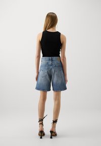 Svart ärmlös topp i kombination med högmidjade, knälånga blå denimshorts. Shorts har en klassisk femficksdesign och fransade kanter.