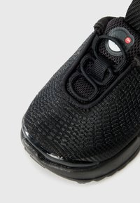 Baskets de sport noires avec une tige en mesh texturé, design sans lacets, détail de logo et semelle rembourrée avec une touche brillante.