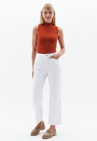 Top arancione aderente senza maniche abbinato a jeans bianchi a vita alta. Mocassini beige con suole spesse per un aspetto casual.