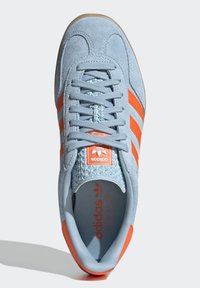 Light blue suede sneaker with orange stripes, textured tongue, and rubber sole. Features logo tag on the tongue and laced design.