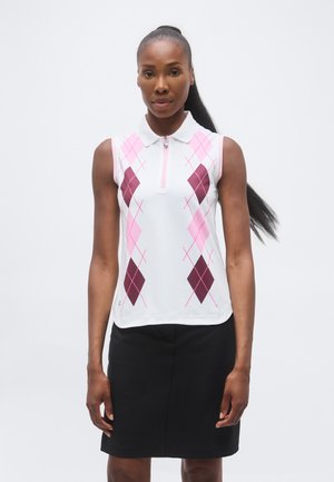 Vrouw draagt een mouwloos wit poloshirt met een roze en bordeaux ruitpatroon en een zwarte rok, staand tegen een effen achtergrond.