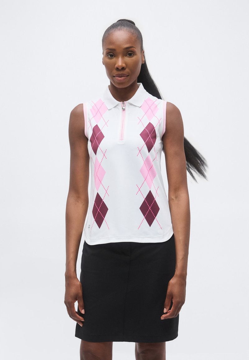 Γυναίκα με λευκό αμάνικο πόλο μπλουζάκι με ροζ και μπορντό αγγελικό σχέδιο και μαύρη φούστα, στέκεται μπροστά σε απλό φόντο.